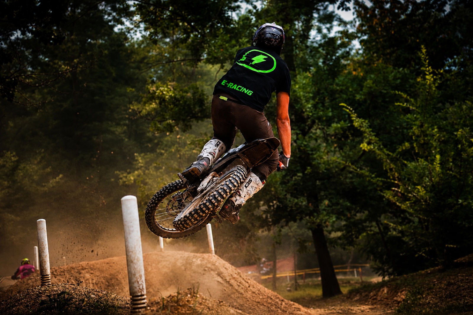 Rider E-Racing in volo sul salto, polvere e sfondo bosco